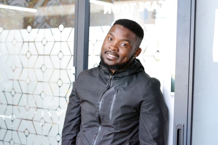 A participant in a dark hooded jacket smiles for the camera outside the meeting room.