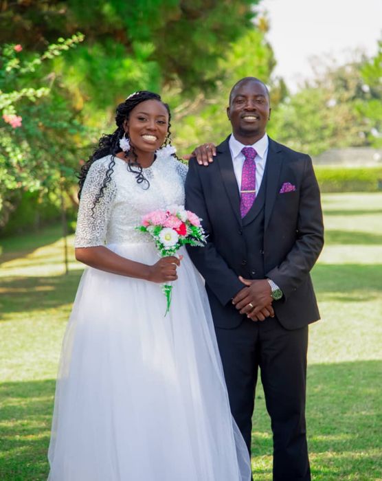 The bride holds a bouquet of pink and white flowers while the groom stands beside her with a hand on her shoulder.