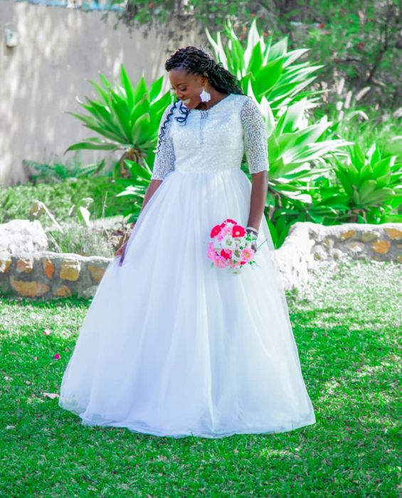 The bride glances down as she holds her bouquet at her side, the full tulle skirt of her gown spread over the grass.