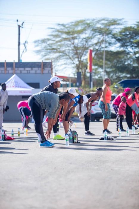 A group of participants bend to stretch in a car park, with water bottles lined up on the ground.