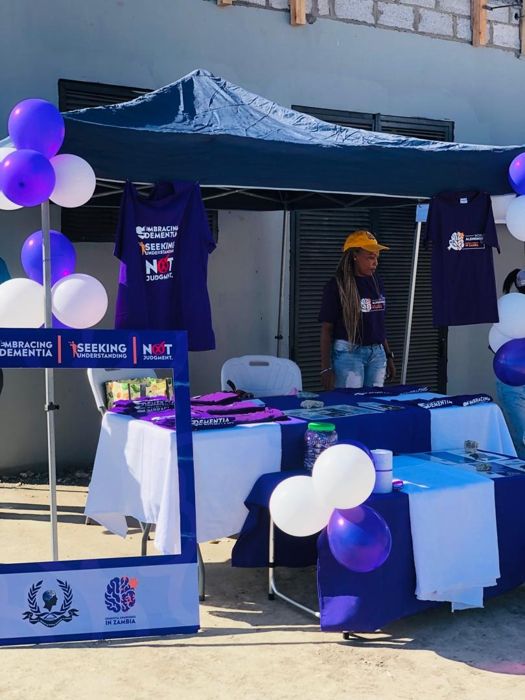 A stand with purple balloons, hanging T-shirts and a photo frame reading “Embracing Dementia, Seeking Understanding, Not Judgment”.